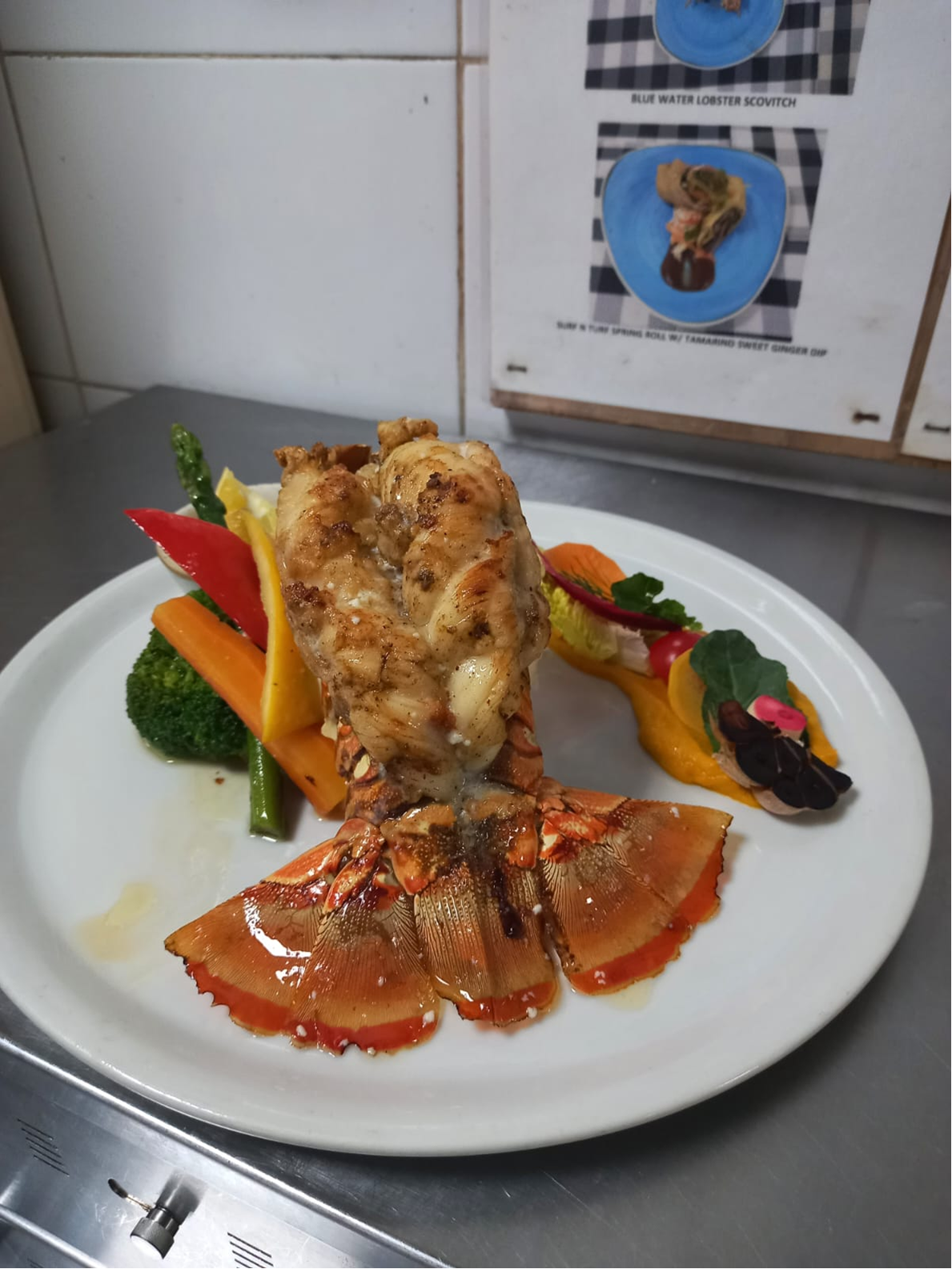 Blue water lobster dish plated with vegetables and bright puree accents.