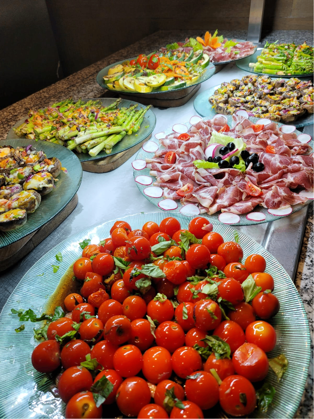 Antipasti buffet with prosciutto, asparagus, tomatoes, mushrooms, and grilled vegetables.